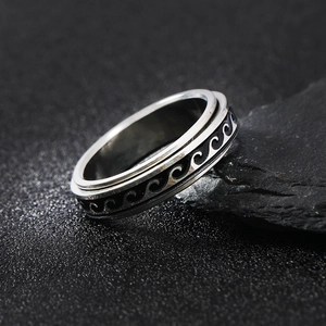 Men's silver stainless steel spinner ring with black wave pattern on dark volcanic rock