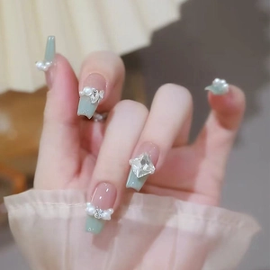 Macro detail of mint green french press-on nails with white pearls and crystal bows