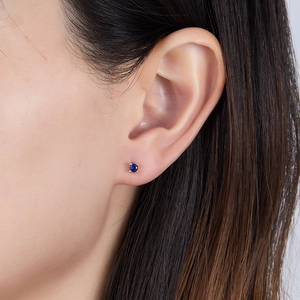 Macro shot of a minimalist gold stud earring with a deep blue zircon on the ear
