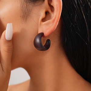 Close-up of minimalist dark brown acrylic C-shaped earring worn by a female model