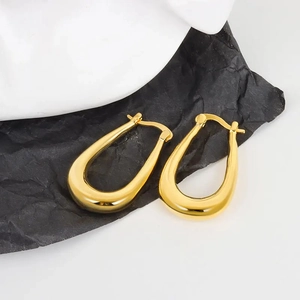 Detailed macro view of polished gold oval U-shaped hoop earrings on black textured paper