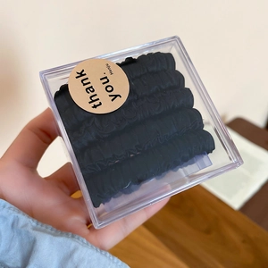 Close-up of five black fabric scrunchies in a clear acrylic box on a wooden table