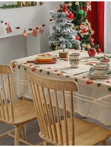 Close-up of beige lace tablecloth with embroidered Christmas bells and holly patterns