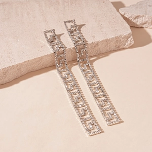 Macro view of silver geometric rhinestone tassel earrings on a textured stone base