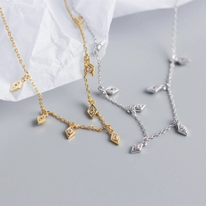 Detailed view of silver and gold geometric rhombic zircon tassel necklaces on white paper