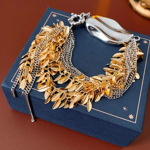 Detail of layered gold leaf tassels and silver fluid charms on a textured chain bracelet