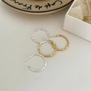 Detailed view of large gold and silver C-shaped earrings with irregular hammered texture