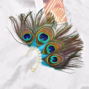 Flat lay of vintage bohemian peacock feather ear cuff with gold alloy hook on white silk