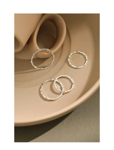 Detailed view of four minimalist S925 silver rings with irregular hammered textures on a plate