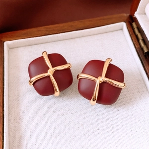 Macro view of vintage burgundy square stud earrings with golden cross knot design