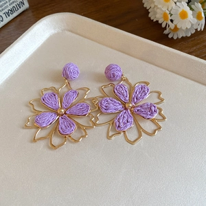 Close-up of purple raffia flower earrings with gold frame on a minimalist beige tray
