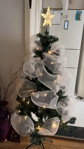 Detail of Christmas tree with green net ribbon, glowing star topper and warm string lights