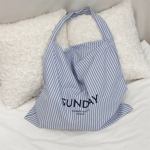 Detail of blue and white striped canvas tote bag with Sunday Summer Night text on a white bed