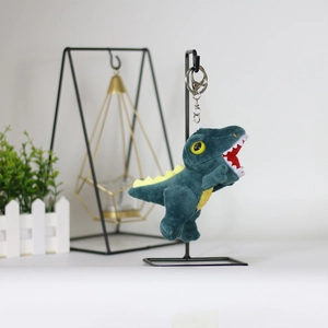 Detail of a dark green plush dinosaur keychain with yellow spikes on a metal stand
