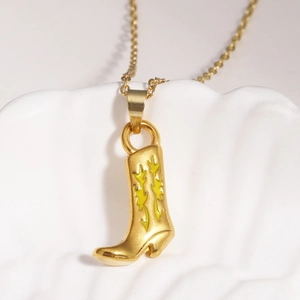 Détail d'un pendentif botte de cowboy dorée avec motifs de flammes jaunes sur une chaîne