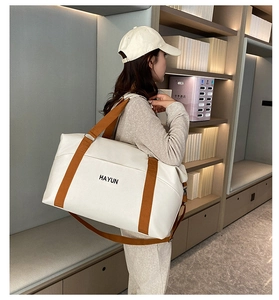 Macro shot of large beige travel tote with brown straps and branding in a cozy room