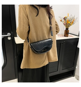 Detail of black leather saddle bag with wide logo strap and gold hardware on model