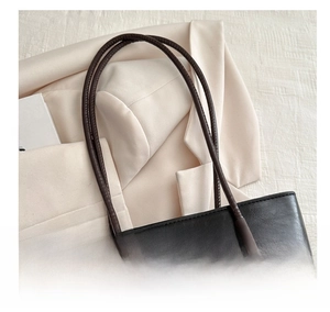 Close-up of black leather tote bag with brown handles showing premium texture
