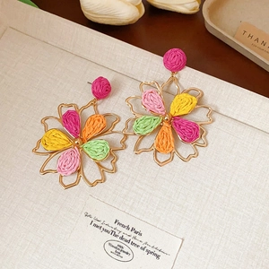 Detail of bohemian raffia drop earrings with colorful floral woven petals in gold frame