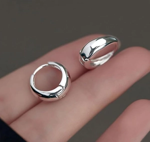 Close-up of polished silver hoop earrings held by hand showing smooth metallic texture