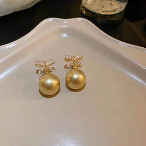 Elegant gold bow earrings featuring pavé cubic zirconia and a large golden pearl drop