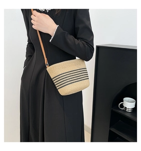 Detail of khaki straw woven bucket bag with black stripes and brown shoulder strap