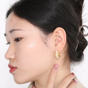 Detailed close-up of a French retro gold C-shaped earring with white pearls on a model