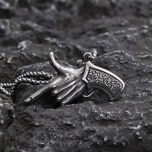 Macro shot of silver pistol gesture pendant on a rugged dark stone surface