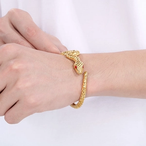 Detailed close-up of golden snake bracelet with red gemstone eyes and scale texture