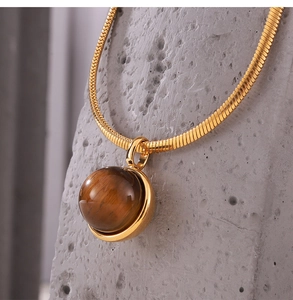 Macro detail of golden snake chain necklace featuring a polished tiger eye stone pendant