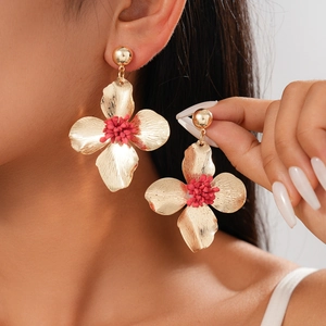 Close-up of golden floral earrings with pink center on model, highlighting metal texture