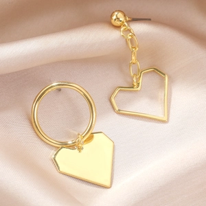 Close-up of asymmetric gold heart earrings with baroque style on champagne satin fabric