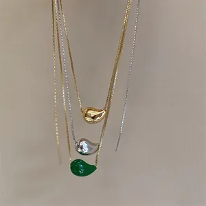 Detailed close-up of teardrop bean pendants in gold, silver, and green on box chains