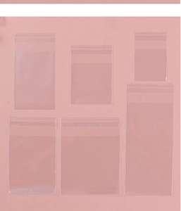 Various sizes of clear self-adhesive plastic packaging bags on a pink background