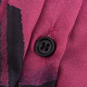 Dettaglio del tessuto twill rosa con motivi neri e bottone in resina a quattro fori
