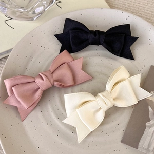 Three elegant ribbon bow hair clips in black, pink, and cream white on ceramic tray