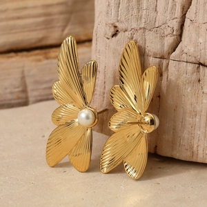 Elegant gold butterfly wing earrings with white pearl detail on a natural stone surface