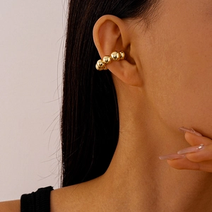 Detail of a minimalist golden beaded C-shaped ear cuff worn on a person's ear