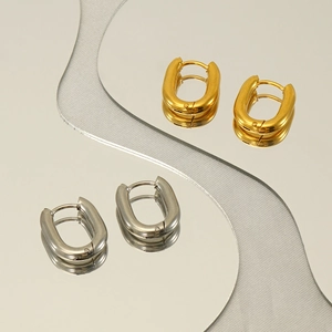 Polished gold and silver oval hoop earrings displayed on a reflective mirror surface