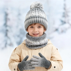 Detail eines Kindes mit grau-weißem Strickset aus Mütze mit Bommel, Schal und Handschuhen
