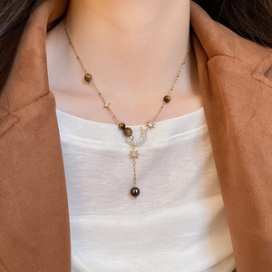 Close-up of golden necklace with tiger eye beads, star-moon pendant and black pearl detail