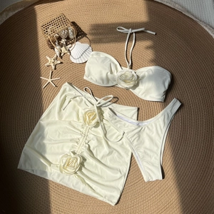 Detailed flat lay of white 3-piece bikini set with 3D rose flowers on a beach themed rug