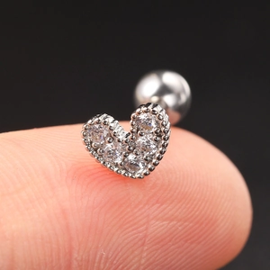 Macro shot of silver heart-shaped zircon piercing earring on a fingertip close-up