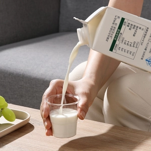 Pouring milk from a 500ml carton into a thick transparent disposable plastic cup