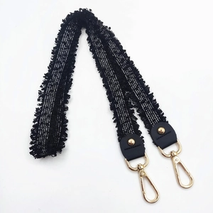 Detail of black tweed shoulder strap with fringe edges and golden metal swivel hooks