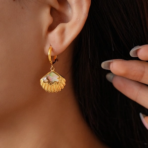 Close-up of a gold shell earring with pearlescent inlay on a model's ear