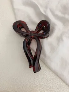 Detail of a large amber tortoiseshell bow hair claw clip on a soft white fabric background