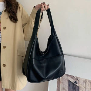 Detail einer großen schwarzen PU-Leder Hobo-Tasche mit Vordertasche gehalten von Model