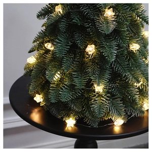 Close-up of a mini Christmas tree with warm yellow LED star lights on a black base