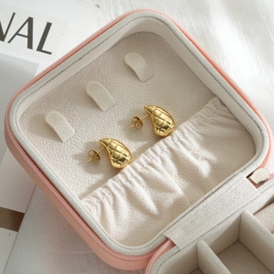 Detail of gold water-drop earrings with quilted texture inside a pink leather jewelry box